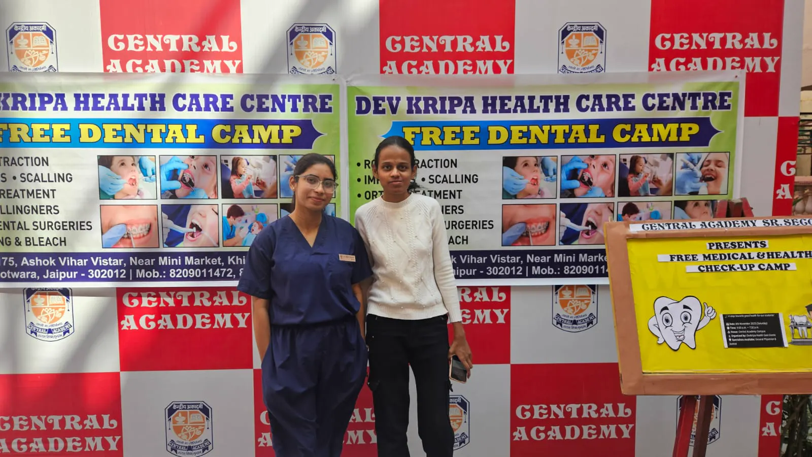Two members of the clinic team in front of the free dental camp banners