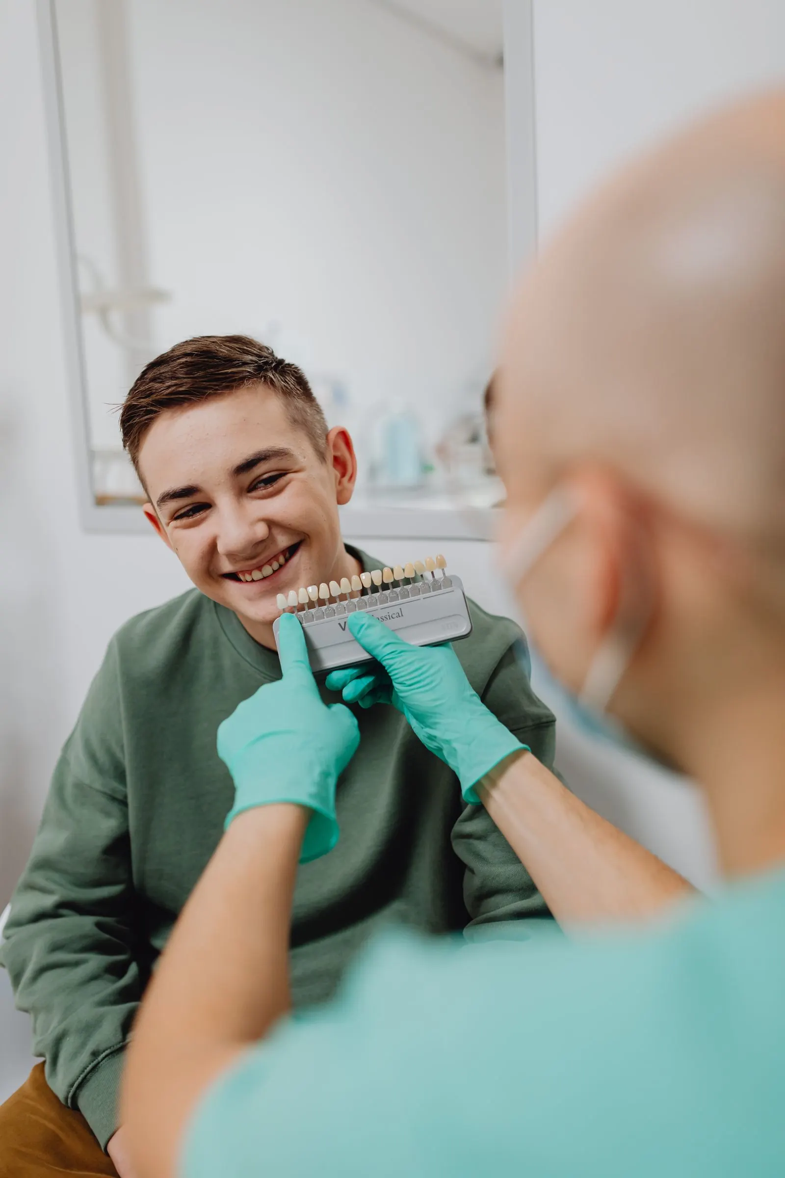 A patient smiling while a dentist holds up a tooth shade guide